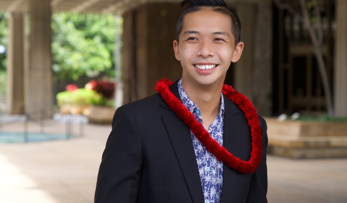 Photo of Adrian Tam smiling and wearing a red lei around his neck