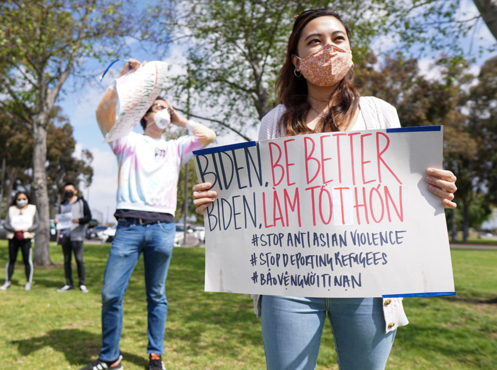 Photo of two people, one of whom holds a sign that says "Biden, be better #STOPANTIASIANVIOLENCE #STOPDEPORTING REFUGEES" as part of a demonstration against the deportation of Southeast Asian refugees