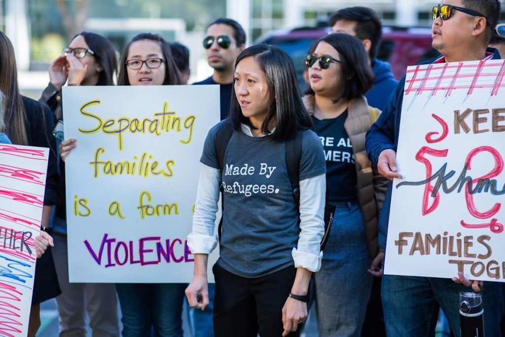Photo of a group of people holding signs that say "Separating families is a form of violence" and "Families together" as part of a demonstration against the deportation of Southeast Asian refugees
