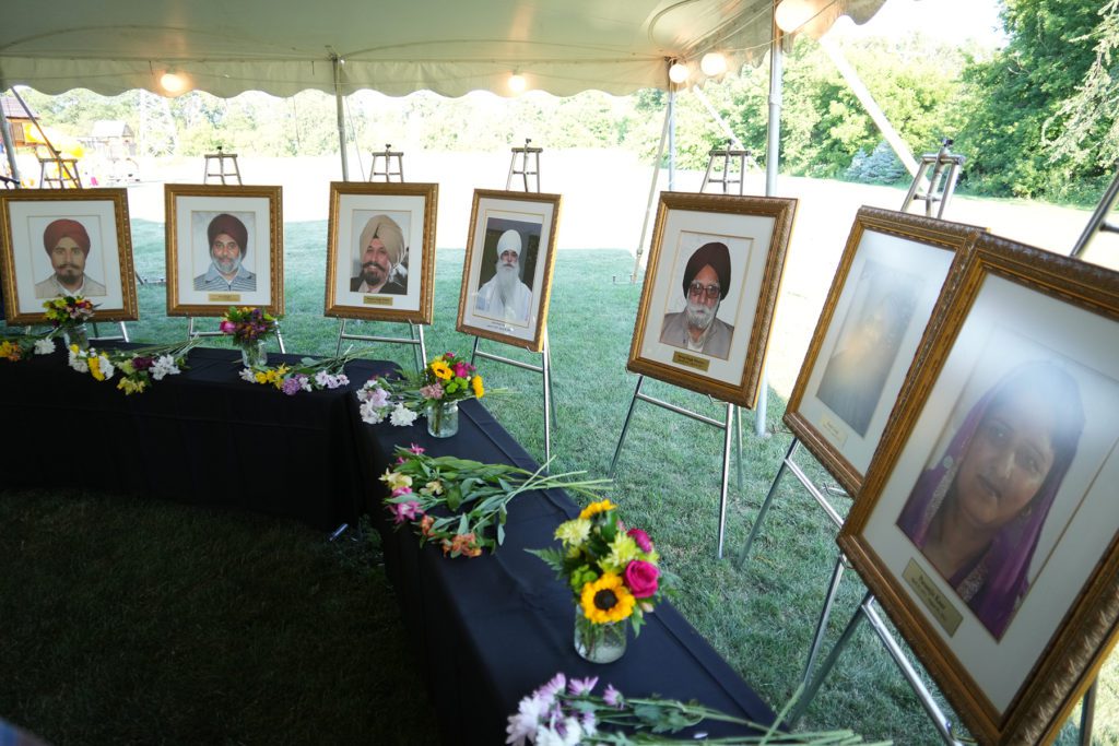 Photo showing the standing portraits of the Sikh Americans who died as a result of the Oak Creek shooting, displayed on a lawn outdoors with flowers laid in front.