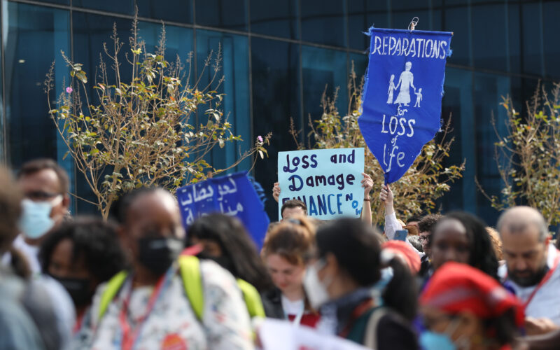 Photo of protesters, including Pacific Islanders, at a rally. The camera is focused on a sign that says "Loss and damage finance now."