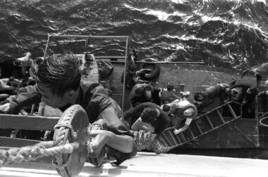 A crewman from the combat stores ship USS SAN JOSE (AFS-7) helps Vietnamese refugees climb from their fishing boat up a Jacobs ladder to the deck of the ship on January 21, 1980. Photo courtesy of The U.S. National Archives and Defense Visual Information Distribution Service.