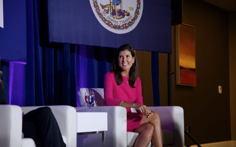 Nikki Haley sits in a white chair on stage at a campaign event.