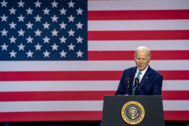 Photo of Joe Biden speaking from a podium as a giant American flag is displayed behind him