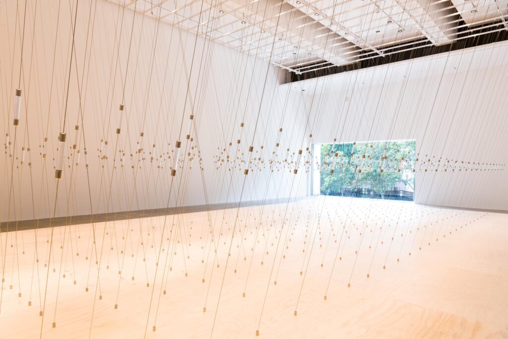 Photo of an art installation showing wires criss-crossing from the ceiling to the floor.