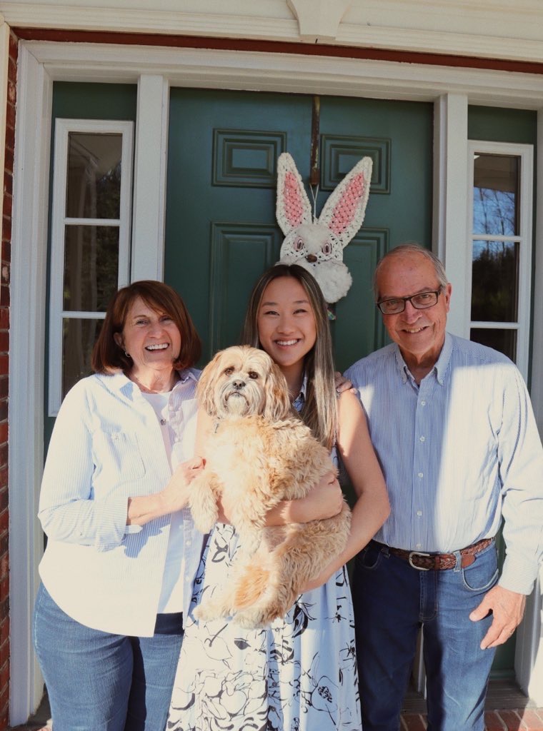 Photo of Annie Wu Henry holding a brown dog as she stands with her parents next to her, one on each side, in front of a green door.
