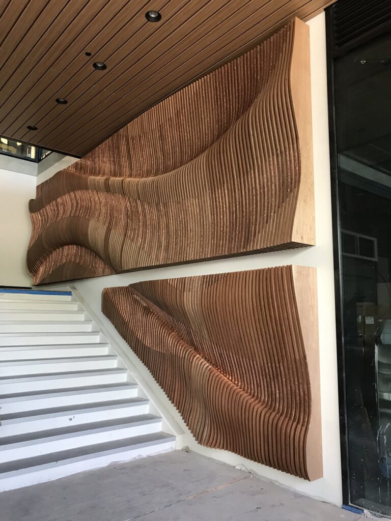 Photo of an art installation showing wooden lines that curve into the shape of a wave next to a staircase.