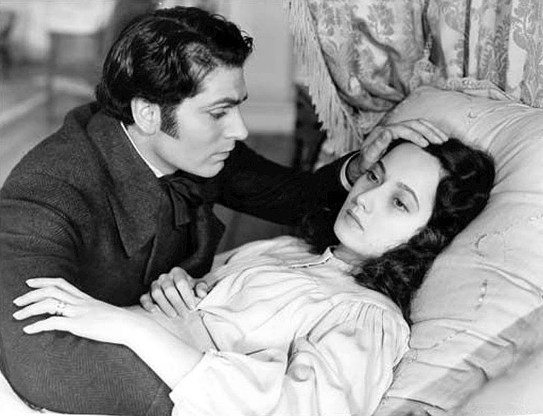 Photo of Laurence Olivier touching Merle Oberon's hair as she lies in bed in a scene from "Wuthering Heights" during Hollywood's early ages