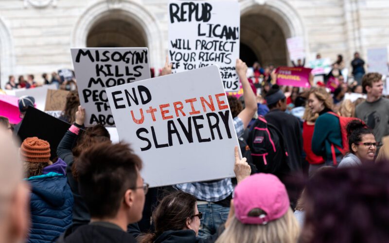 Demonstrators hold up signs including one that says "End Uterine Slavery."