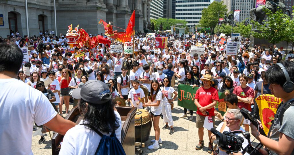 Photo of a crowd of protesters holding up signs and banners as they rally in front of Philadelphia City Hall to protest plans to build an arena in Chinatown