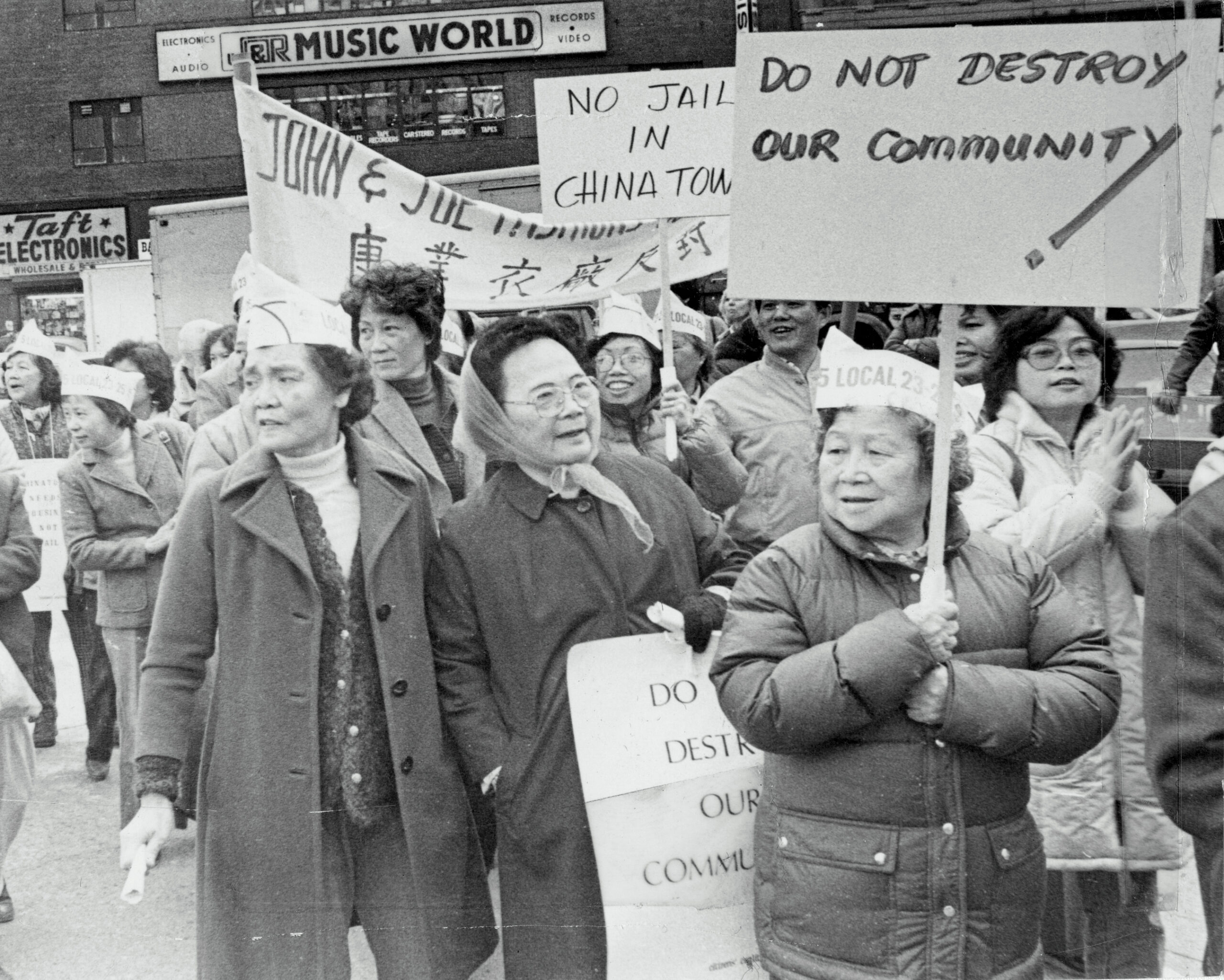 Black-and-white photo of Manhattan Chinatown residents holding signs that protest the reopening of the Tombs building 