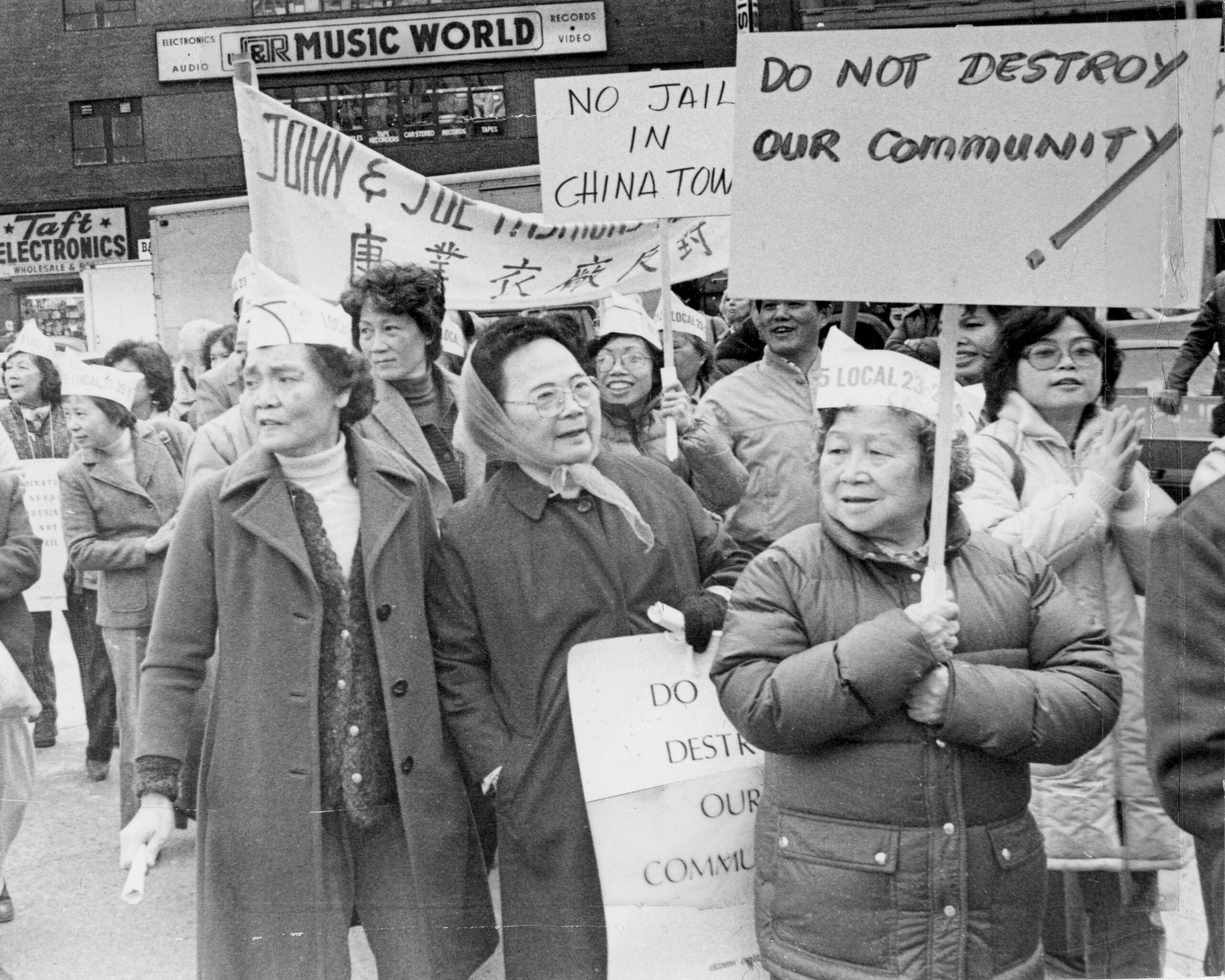 Black-and-white photo of Manhattan Chinatown residents holding signs that protest the reopening of the Tombs building