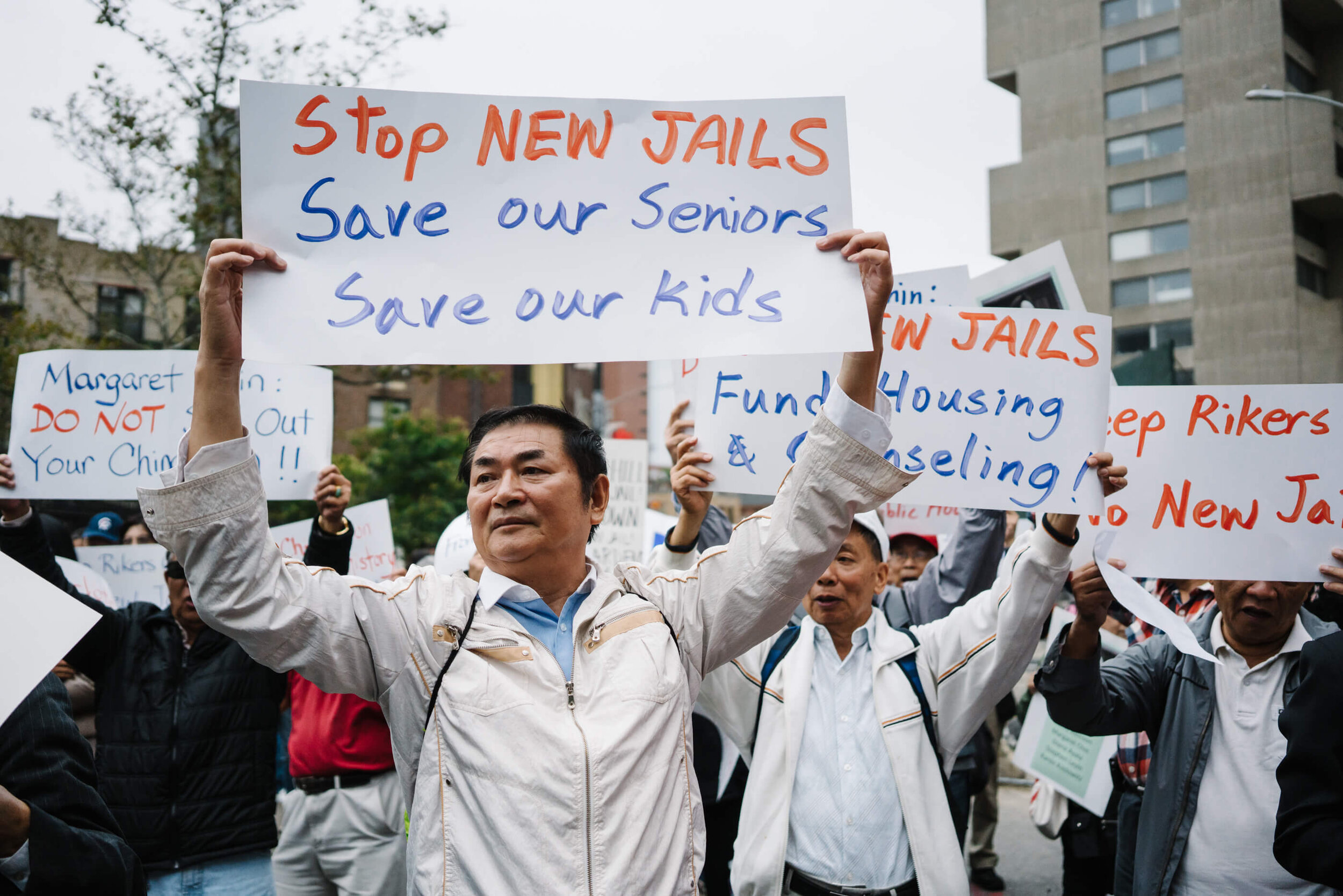 Photo of Manhattan Chinatown residents holding up signs that say: "Stop new jails, save our seniors, save our kids"