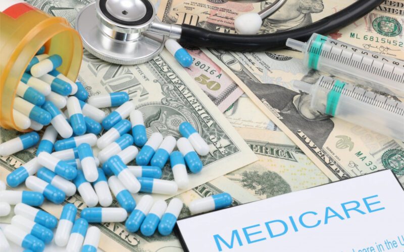 Photo of medication pills splayed on top of dollar bills and a piece of paper that says "Medicare."