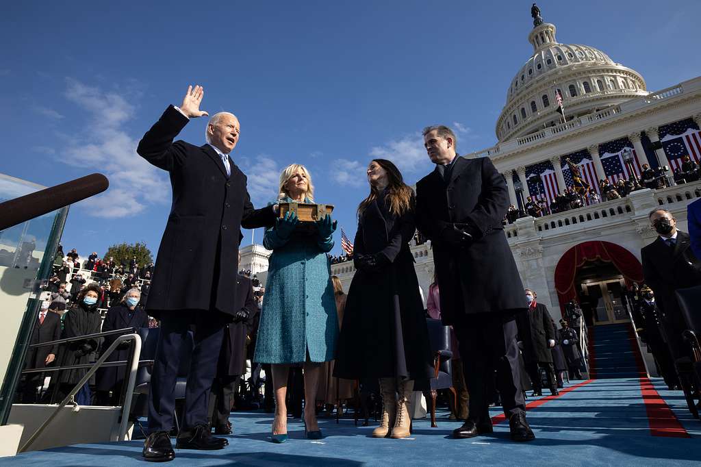 Photo of Joe Biden raising his right hand as he is sworn into office in front of the U.S. Capitol. Jill Biden holds the Bible his left hand is resting on while their two adult children watch on from their left.