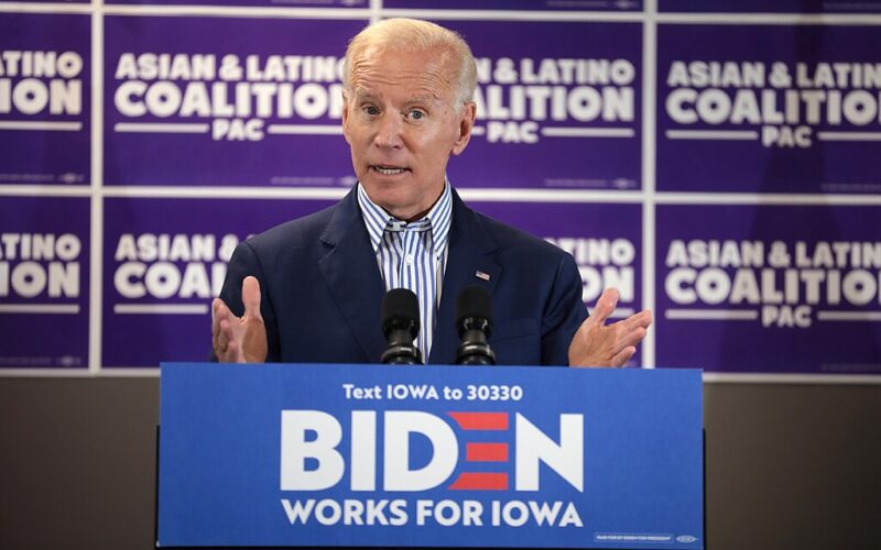 Photo of Joe Biden speaks from a podium at a town hall. The wall behind says "Asian & Latino Coalition."