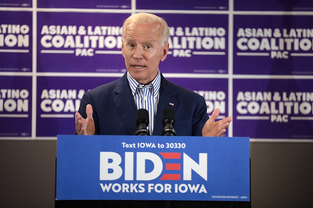 Photo of Joe Biden speaks from a podium at a town hall. The wall behind says "Asian & Latino Coalition."