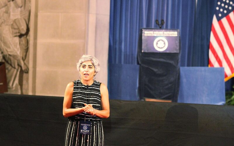Photo of Kiran Ahuja speaking in front of a stage