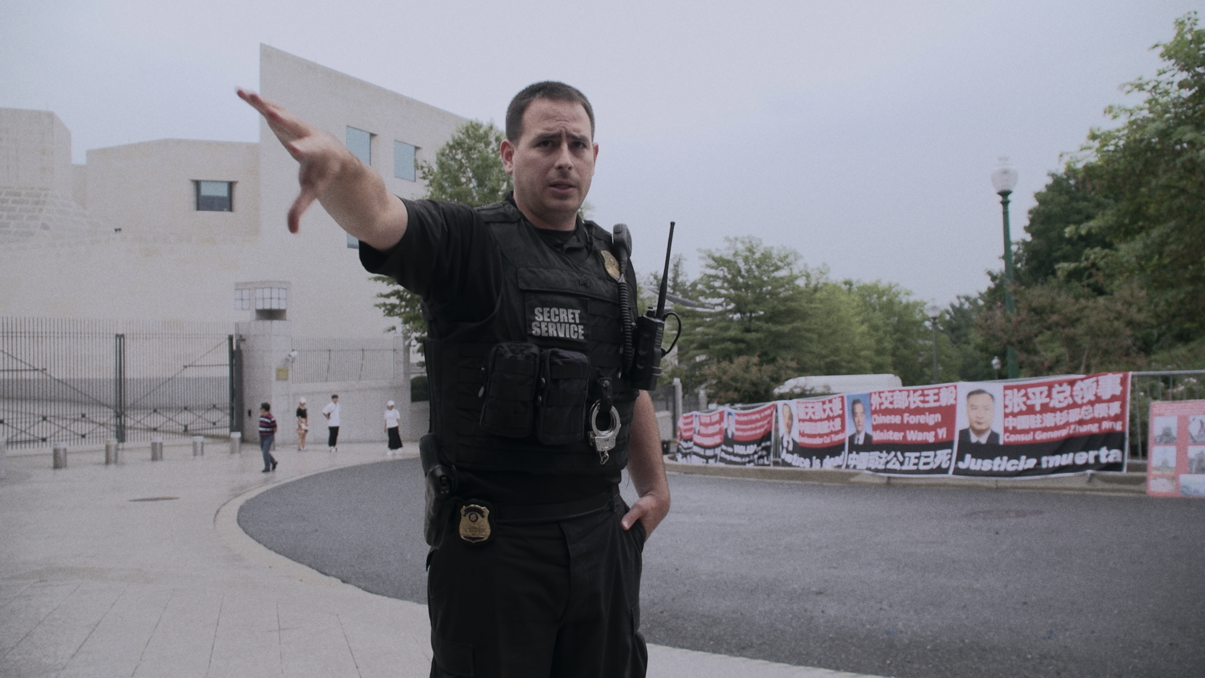 Photo of a police officer gesturing at the camera as an anti-CCP rally takes place behind