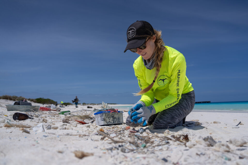 Photo of a marine debris technician kneeling on the sand to collect plastics buried in the sand