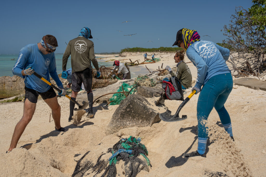 Photo of three workers digging up sand covering marine debris
