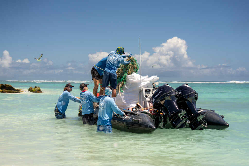 Photo of people loading a huge white bag of marine debris into a small black boat