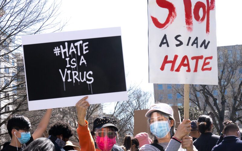Photo of two protesters holding signs that say "#HateIsAVirus" and "Stop Asian Hate"
